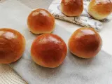 Pięć puszystych bułek maślanych, lśniących od pieczenia, ułożonych na lnianej serwetce.