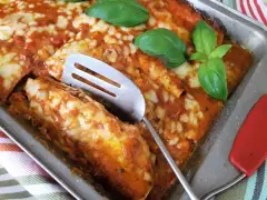 Zapiekana tortilla z mięsem mielonym, polana sosem pomidorowym i posypana serem, ozdobiona listkami bazylii.