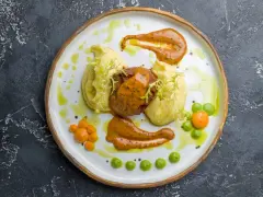 Mięso z puree ziemniaczanym, ozdobione pomarańczowym sosem do mielonych i zielonymi groszkami.