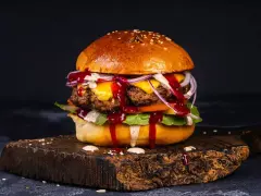 Soczyste burgery z grilla, polane sosem, z serem, cebulą i sałatą, na drewnianej desce.