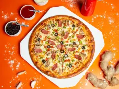 Pizza z kiełbasą, pieczarkami i oliwkami na pomarańczowym tle, obok sosy i imbir.