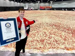Mężczyzna prezentuje certyfikat Guinnessa za największą pizzę świata, która rozciąga się na ogromnej przestrzeni.