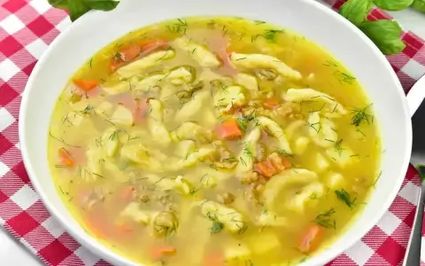 Aromaticzna zupa zacierkowa z kawałkami marchewki i świeżym koperkiem, podana w białej misce na czerwono-białej kratce.