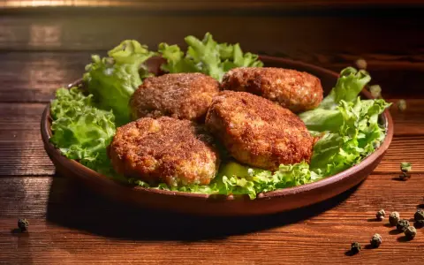 Cztery apetyczne kotlety mielone z airfryer, podane na liściach sałaty. Idealne na szybki obiad.