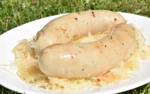 Dwie pyszne kiszki ziemniaczane na grilla, podane na talerzu z kapustą kiszoną. Idealne na letnie popołudnie.