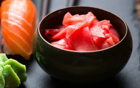 Miseczka z różowym, marynowanym imbirem obok sushi i wasabi. Idealny dodatek do japońskich potraw.