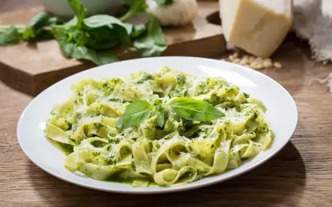 Talerz tagliatelle z aromatycznym pesto z rukoli, posypany parmezanem i udekorowany listkami bazylii.