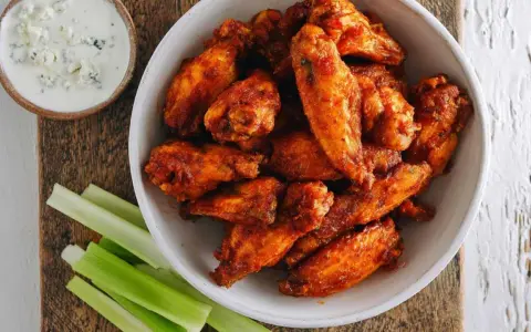 Chrupiące skrzydełka z airfryer w misce, obok sosu serowego i łodyg selera. Idealna przekąska!