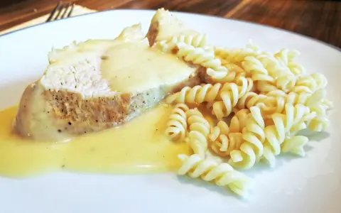Kawałek pieczonego mięsa w kremowym sosie potrawkowym, podany z makaronem fusilli.