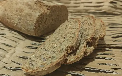 Chleb orkiszowy, pokrojony na kromki, z widocznymi ziarnami, leży na falistej tekturze.