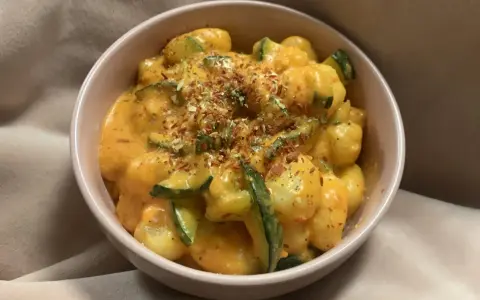 Puszyste gnocchi z cukinią w kremowym sosie, posypane ziołami i płatkami chili. Pyszne gnocchi z pesto w miseczce.