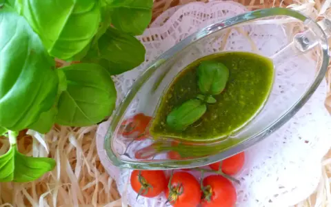 Świeże liście bazylii i pomidorki koktajlowe obok sosu pesto z bazylii w szklanym naczyniu.