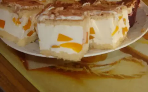 Sernik z bitą śmietaną siostry Anastazji, z kawałkami brzoskwini, posypany kakao. Pyszny deser na talerzu.