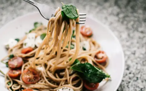 Widelec podnosi porcję spaghetti z pomidorkami i mozzarellą. Czy makaron to węglowodany? Tak, to pyszne źródło energii!