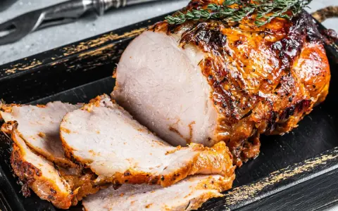 Soczysty schab pieczony w piekarniku w naczyniu, pokrojony w plastry, ozdobiony gałązką rozmarynu.