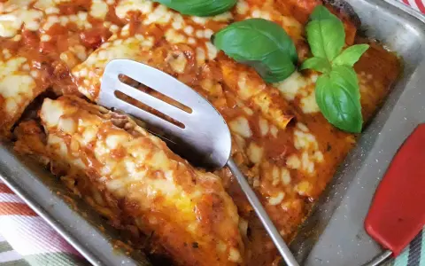 Zapiekana tortilla z mięsem mielonym, polana sosem pomidorowym i posypana serem, ozdobiona listkami bazylii.