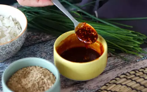 Łyżka z aromatycznym sosem gochujang, obok miseczki ryżu, sezamu i szczypiorku.
