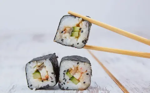 Trzy kawałki sushi z ryżem, ogórkiem i rybą, jeden podniesiony pałeczkami. Idealne do sosu, który stanowi zalewa do sushi.