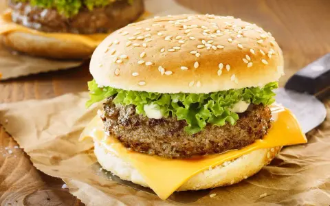 Zbliżenie na cheeseburgera z serem, sałatą i majonezem na bułce z sezamem.