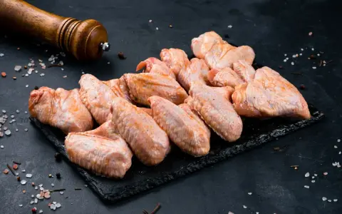 Skrzydełka kurczaka gotowe do pieczenia, zamarynowane w aromatycznej solance. Obok młynek do pieprzu i gruboziarnista sól.