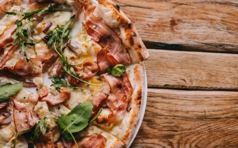 Pyszna pizza carbonara z chrupiącym boczkiem i rukolą, podana na drewnianym blacie.