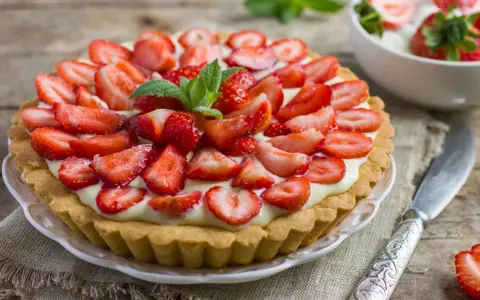 Tarta z truskawkami i kremem, ozdobiona listkami mięty.
