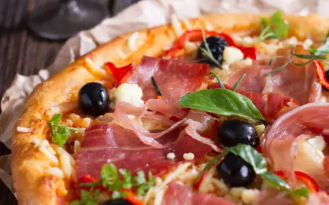 Pyszna pizza z cienko pokrojoną, aromatyczną szynką, czarnymi oliwkami i papryką. Idealna jaka szynka na pizzę!