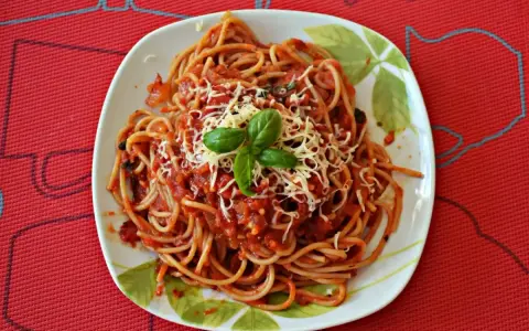 Pyszny sos do makaronu spaghetti z tartym serem i bazylią na talerzu.