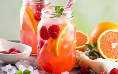 Orzeźwiająca lemoniada malinowa z pomarańczą i miętą w słoikach, podana z kostkami lodu.