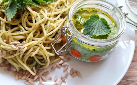 Makaron z pesto z pokrzywy, ozdobiony świeżymi liśćmi pokrzywy i pestkami słonecznika. Obok słoiczek z domowym pesto.
