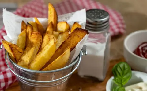 Złociste frytki w metalowym wiaderku, obok solniczka i ketchup. Czy ziemniaki sałatkowe nadają się na frytki? Wyglądają pysznie!