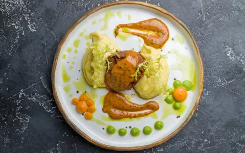 Mięso z puree ziemniaczanym, ozdobione pomarańczowym sosem do mielonych i zielonymi groszkami.