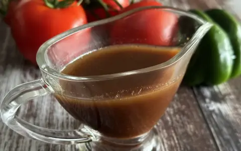 Sos balsamiczny w sosjerce, w tle pomidory i zielona papryka. Idealny do sałatek i mięs.