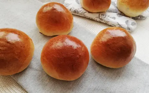 Pięć puszystych bułek maślanych, lśniących od pieczenia, ułożonych na lnianej serwetce.