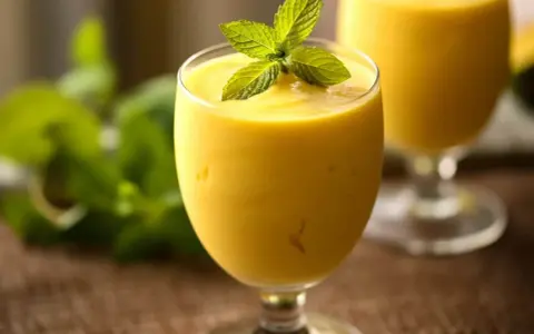 Orzeźwiający koktajl z mango, udekorowany listkami mięty, w szklance na nóżce. W tle drugi taki sam napój.