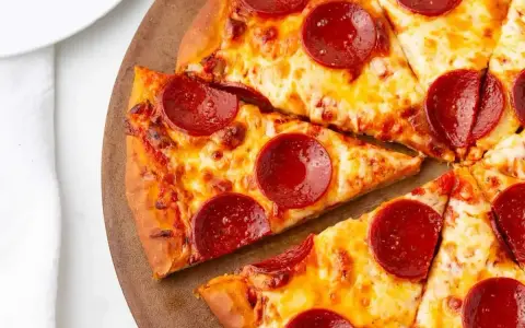 Kawałki pizzy z serem i okrągłymi plasterkami peperoni, ułożone na drewnianej desce.