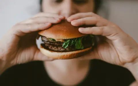 Osoba trzyma soczystego burgera, zastanawiając się, ile kalorii ma burger w restauracji.