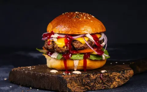 Soczyste burgery z grilla, polane sosem, z serem, cebulą i sałatą, na drewnianej desce.