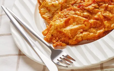Złocisty kotlet słoneczny na białym talerzu, obok sztućce. Idealny na słoneczny dzień.