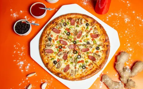 Pizza z kiełbasą, pieczarkami i oliwkami na pomarańczowym tle, obok sosy i imbir.