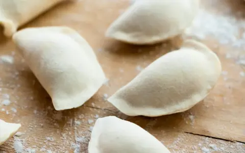 Surowe pierogi uformowane na drewnianej desce. To ciasto na pierogi bez jajka, gotowe do nadzienia.