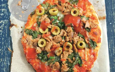 Pyszna pizza z tuńczykiem, szpinakiem i oliwkami, gotowa do pokrojenia.