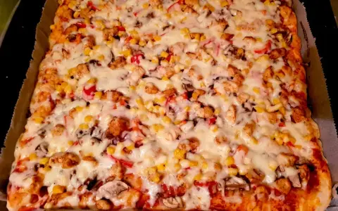 Pyszny przepis na pizzę z kurczakiem, kukurydzą i pieczarkami, obficie posypaną ciągnącym się serem.