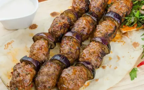 Kofta kebab z bakłażanem na płaskim chlebie, podany z sosem.