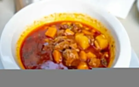 Zupa gulaszowa Ani gotuje się w głębokim talerzu. Mięso i ziemniaki w aromatycznym, czerwonym sosie.