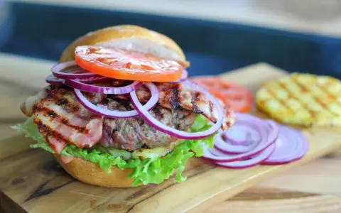 Soczysty burger z chrupiącym boczkiem, pomidorem, sałatą i czerwoną cebulą. Dodatki do burgera kuszą smakiem.
