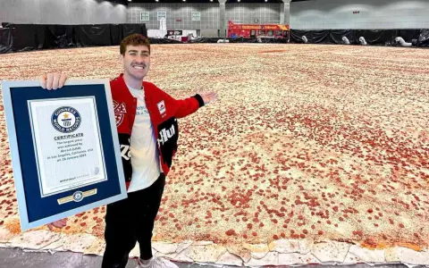 Mężczyzna prezentuje certyfikat Guinnessa za największą pizzę świata, która rozciąga się na ogromnej przestrzeni.