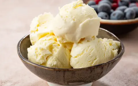 Pyszne, kremowe domowe lody waniliowe w miseczce, obok miseczka z jagodami i malinami.