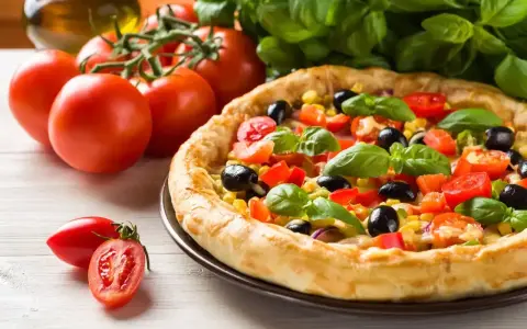 Pyszna pizza z pomidorami, oliwkami i kukurydzą, obok świeże pomidory i bazylia. Ile piec pizze?