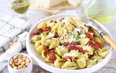 Pyszny makaron z pesto i suszonymi pomidorami, posypany parmezanem i orzeszkami pinii.